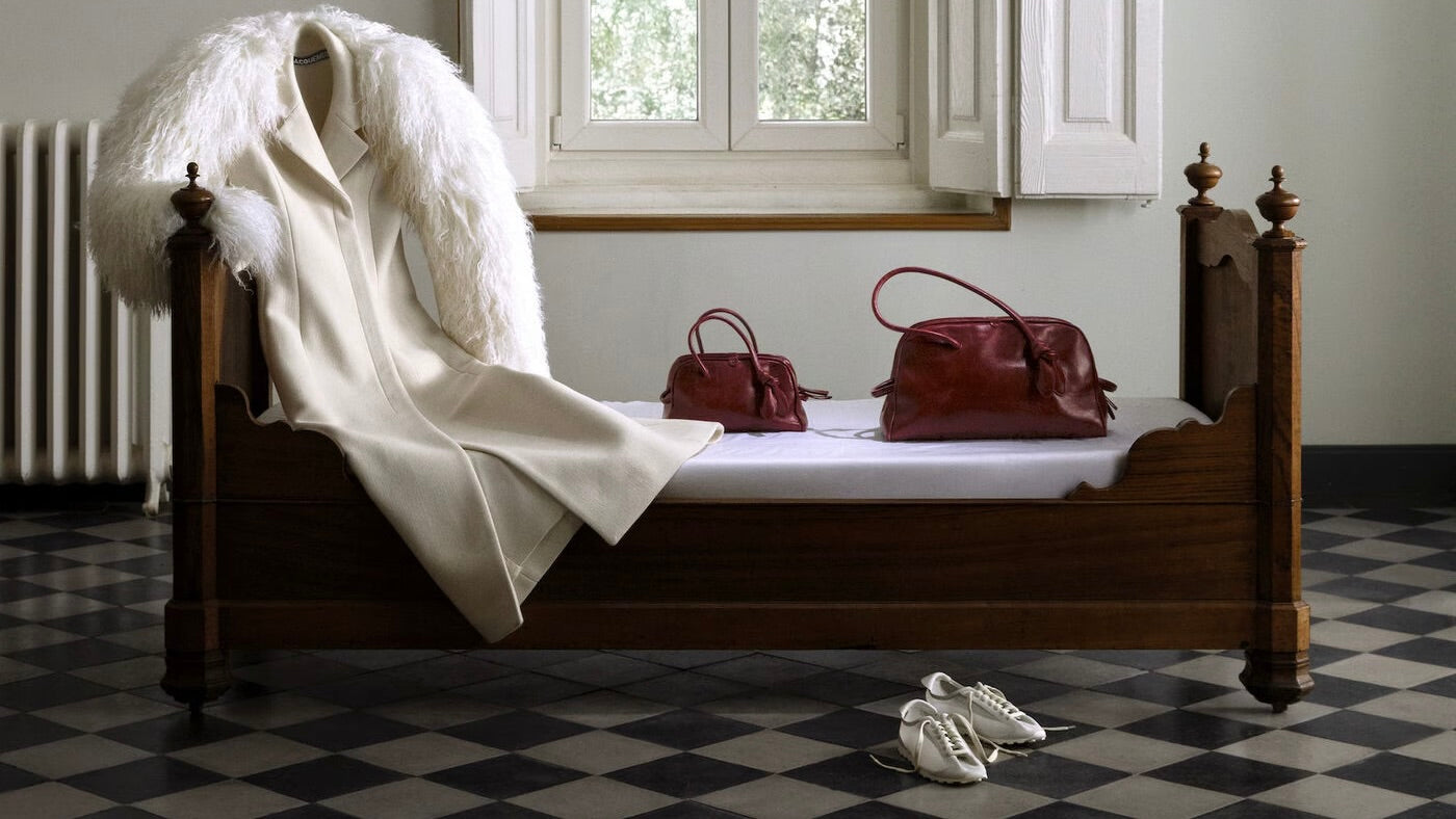 Wooden bed with white bedding, two red bags, and a white garment on a checkered floor.