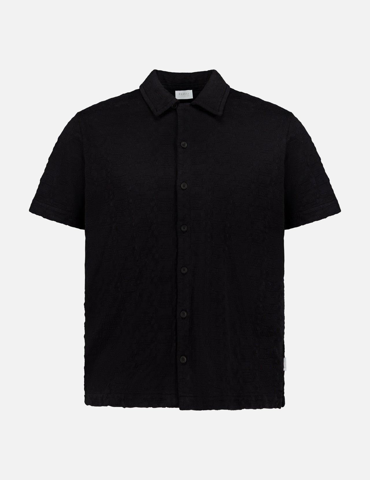 The Abstract Jersey Cuba Shirt by 04651/ A TRIP IN A BAG is a lightweight cotton, short-sleeve, button-up black shirt with a classic Cuban collar, shown against a plain white background.