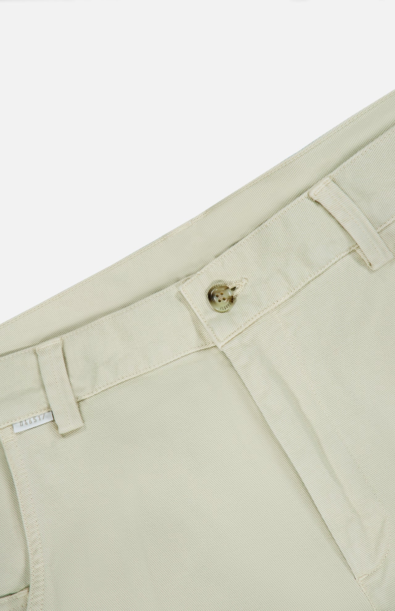 Close-up of the Bull Denim 5-Pocket Pants by 04651/ A TRIP IN A BAG, highlighting the light beige waistband, button, belt loops, small white size tag, and the top of a pocket against a white background.