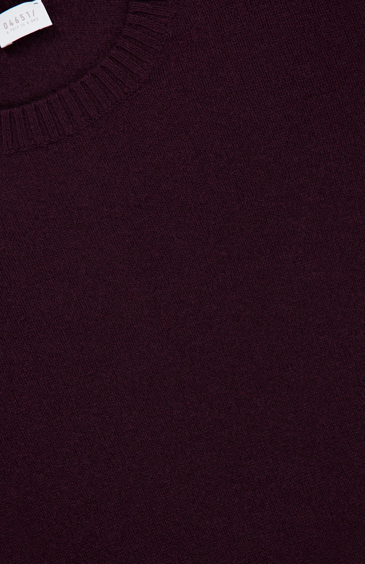 Close-up of the 04651/ A TRIP IN A BAG Extreme Cashmere Crewneck Sweater in dark maroon, featuring a ribbed crew neckline and a small white tag in the top left corner, elegantly highlighting its exquisite “made in Italy” craftsmanship.