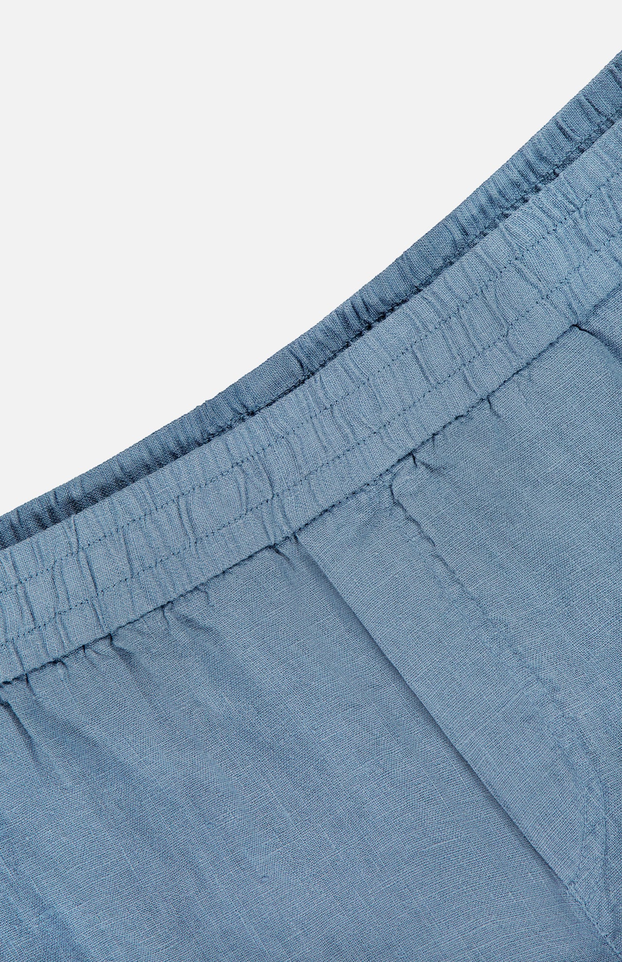 Close-up of the waistband and upper section of the Linen Bermuda Short by 04651/ A TRIP IN A BAG, crafted in Portugal from light blue linen. Features an elastic waist and visible stitching for a soft, lightweight, comfortable fit.