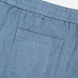 Close-up of the Linen Bermuda Short by 04651/ A TRIP IN A BAG, showing the back with a light blue linen fabric, elastic waistband, and single right patch pocket. Made in Portugal. Displayed against a plain white background.