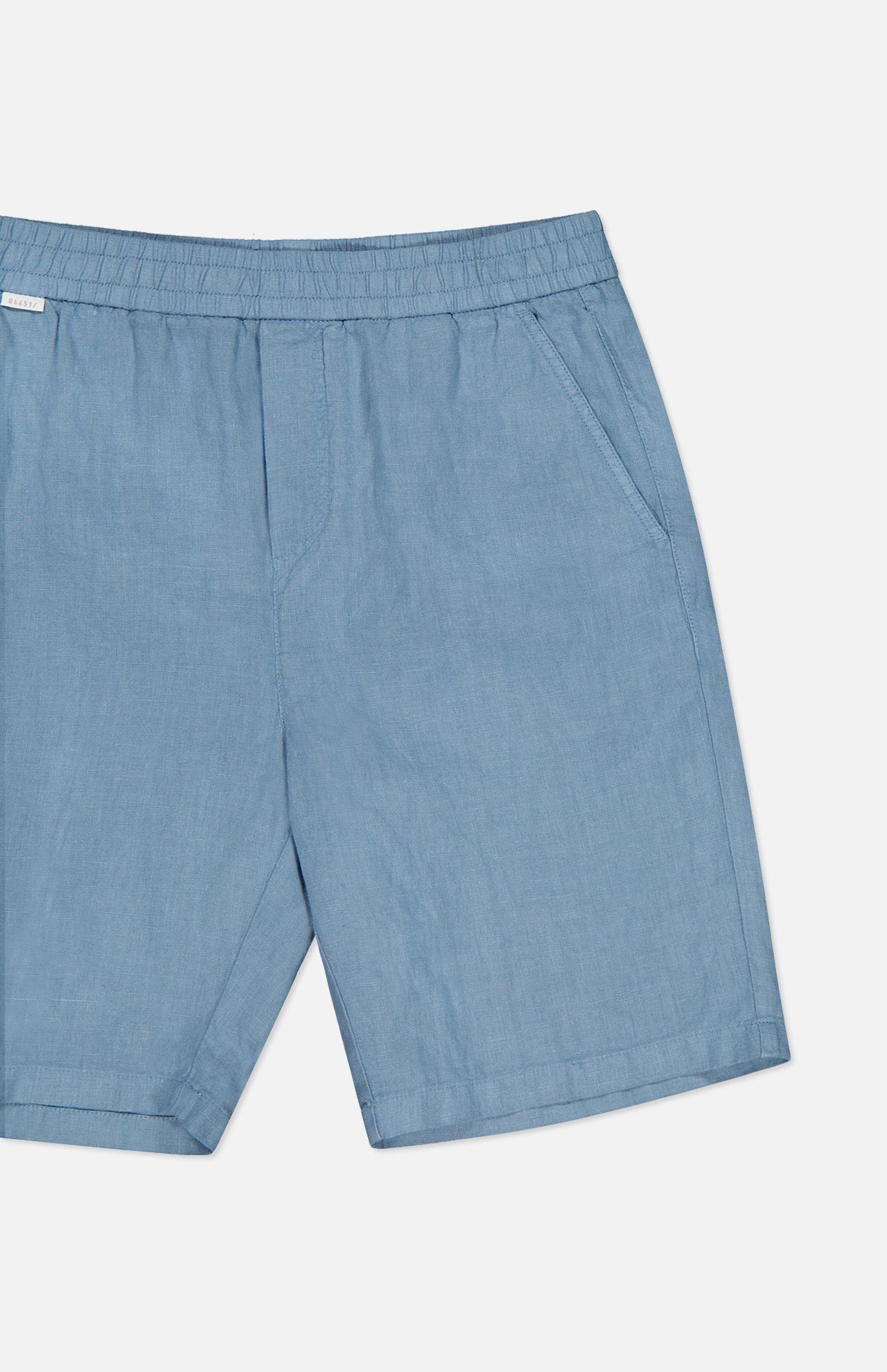 The Linen Bermuda Short by 04651/ A TRIP IN A BAG features light blue linen, an elastic waistband, and side pockets. Made in Portugal, it is displayed on a plain white background.
