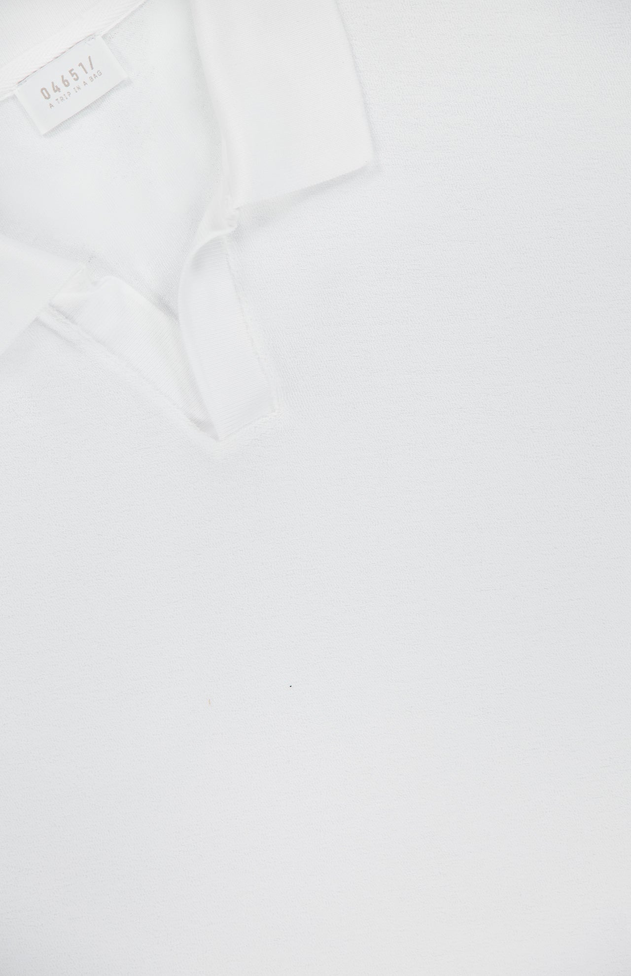Close-up of the Terry Johnny Long Sleeve Collar Polo Shirt by 04651/ A TRIP IN A BAG, clean and laid flat on a white background, with part of the shirt and neck tag featuring a number and text visible.