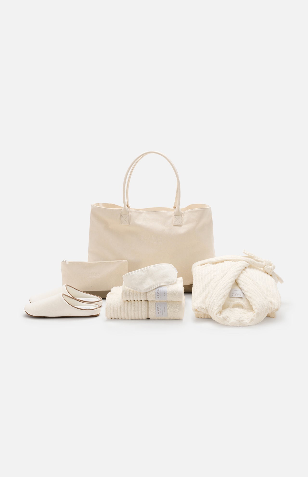 The Voyage Set Tote Bag by 04651/ A TRIP IN A BAG, along with a matching zip pouch, folded towels, cozy slippers, and a folded waffle robe tied with a bow, are arranged neatly on a white background.