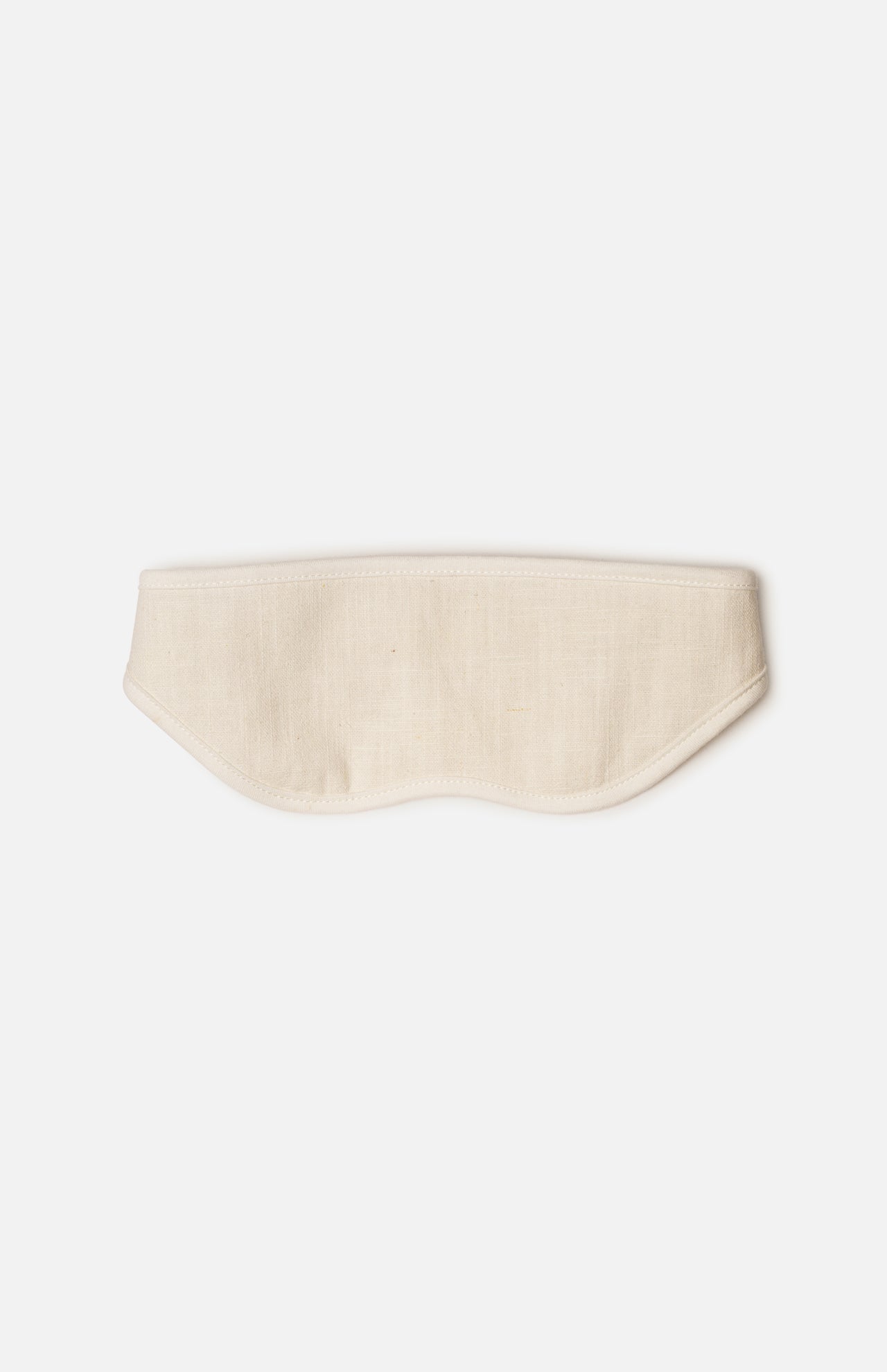 A beige fabric sleep mask with stitched edges and a gentle, contoured shape rests on a white background—perfect for slipping into your Voyage Set Tote Bag by 04651/ A TRIP IN A BAG, making it an essential companion for restful journeys.