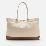 The Voyage Set Tote Bag by 04651/ A TRIP IN A BAG is a spacious beige canvas shopper with dual handles and a brown base, shown against a plain white background—a versatile travel essential perfect for everyday use.