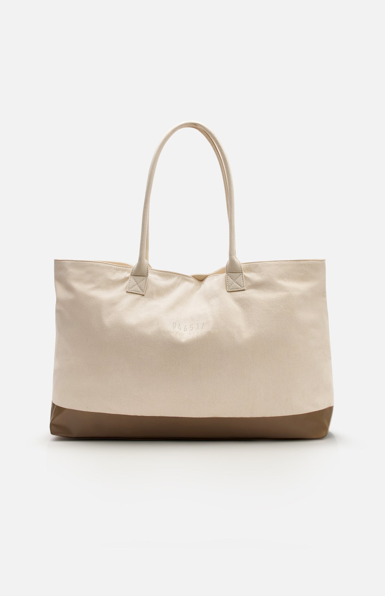 The Voyage Set Tote Bag by 04651/ A TRIP IN A BAG is a spacious beige canvas shopper with dual handles and a brown base, shown against a plain white background—a versatile travel essential perfect for everyday use.