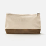 A beige zippered pouch with a brown base, photographed against a white background, features the subtle 04651/ A TRIP IN A BAG branding embossed on the upper front—an understated accessory from the Voyage Set Tote Bag collection, ideal for organizing small essentials in your travel tote.