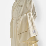 A man wearing glasses and a white textured bathrobe with “Voyage” embroidered on the chest holds the Voyage Set Tote Bag from 04651/ A TRIP IN A BAG—a true travel essential. The background is plain white.