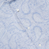 Close-up of the 100 HANDS Jacquard Paisley Dress Shirt in light blue, featuring a subtle paisley pattern, white buttons, and a visible collar with the signature label. The textured linen adds to its refined appeal.