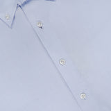 Close-up of the 100 HANDS Oxford Casual Fit Shirt in light blue cotton, featuring white buttons. The shirt is neatly pressed and laid flat, displaying its smooth yet subtly textured fabric. A visible collar and part of the shirt label are shown in the top left corner. This handmade piece exemplifies 100 HANDS’s commitment to craftsmanship and meticulous attention to detail.