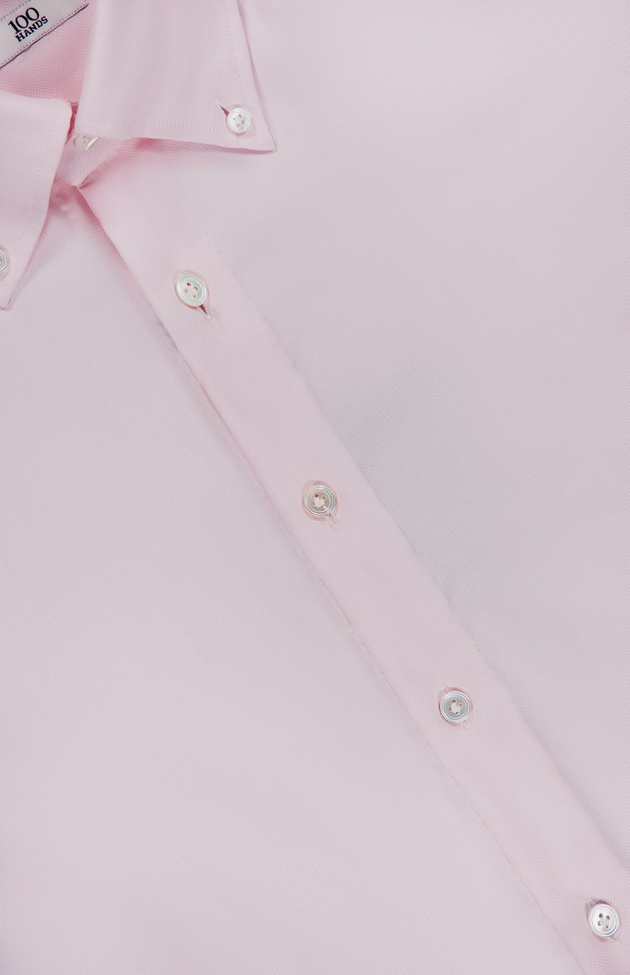 A close-up of the 100 HANDS Oxford Casual Fit Shirt, crafted in India from luxurious light pink cotton, features a pointed collar, white buttons, and is laid flat to showcase its exquisite texture and meticulous stitching.