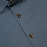 Close-up of the 100 HANDS Seersucker Dress Shirt in textured blue fabric, brown buttons, and a white collar label with "100". The shirt is neatly pressed and has subtle patterns, showcasing quality craftsmanship from India.
