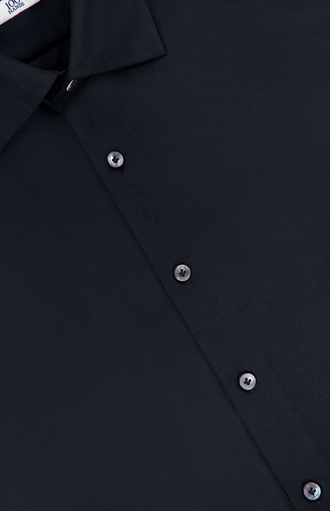 Close-up of the 100 HANDS Silk Casual Fit Dress Shirt in black, highlighting the collar, five black buttons, and a section of the front panel. The smooth, matte silk fabric exemplifies the refined craftsmanship characteristic of every shirt from 100 HANDS.