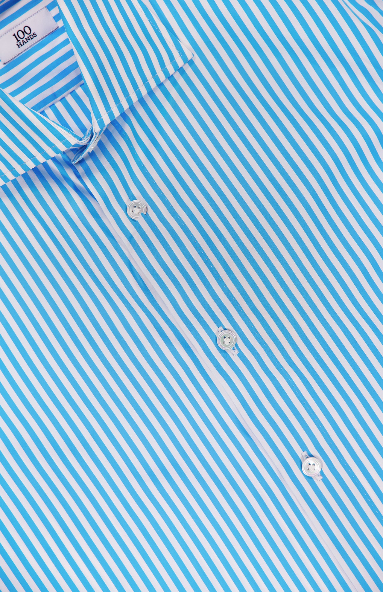 A close-up of the 100 HANDS Stripe Cotton Shirt shows blue stripes, white buttons, and a crisp collar with a "100" label, underscoring the classic style and quality craftsmanship of this 100% cotton shirt.