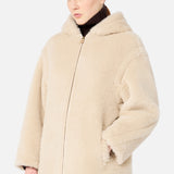 A woman wearing a Max Mara Teddy Hooded Coat in beige over a dark brown turtleneck.