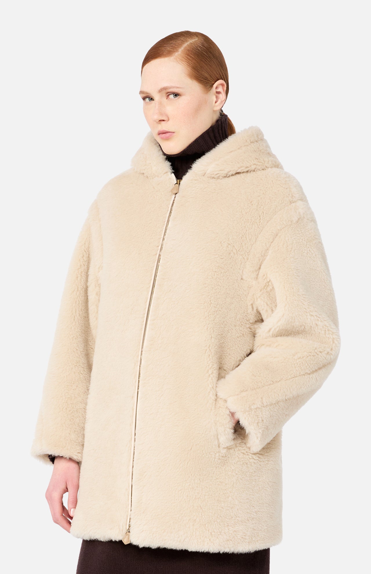 A woman wearing a Max Mara Teddy Hooded Coat in beige over a dark brown turtleneck.
