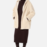 A person wearing a beige Max Mara Teddy Hooded Coat over a dark brown sweater dress, dark tights, and lace-up boots, with dark sunglasses.