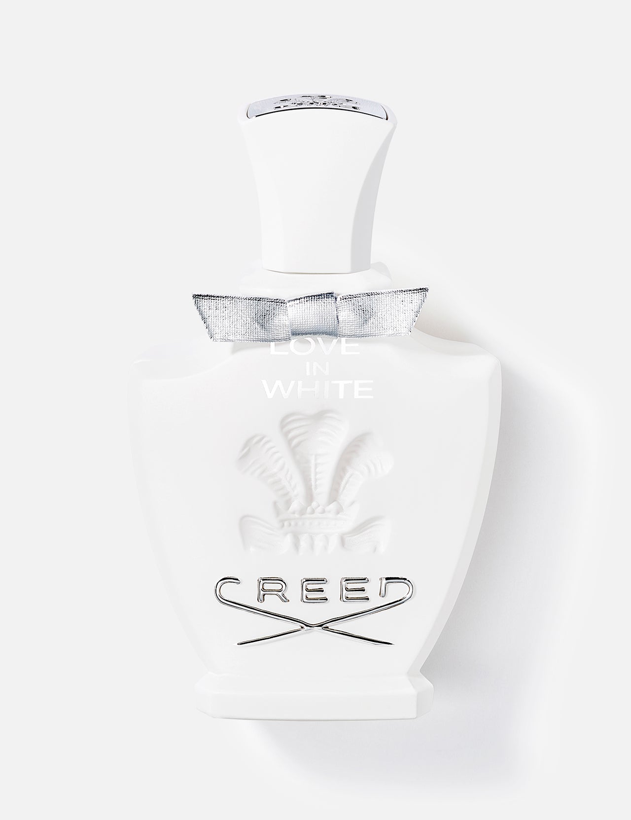 A white 75ml bottle of CREED Love In White fragrance features an embossed crest, silver bow, and black lettering, displayed against a plain light background.