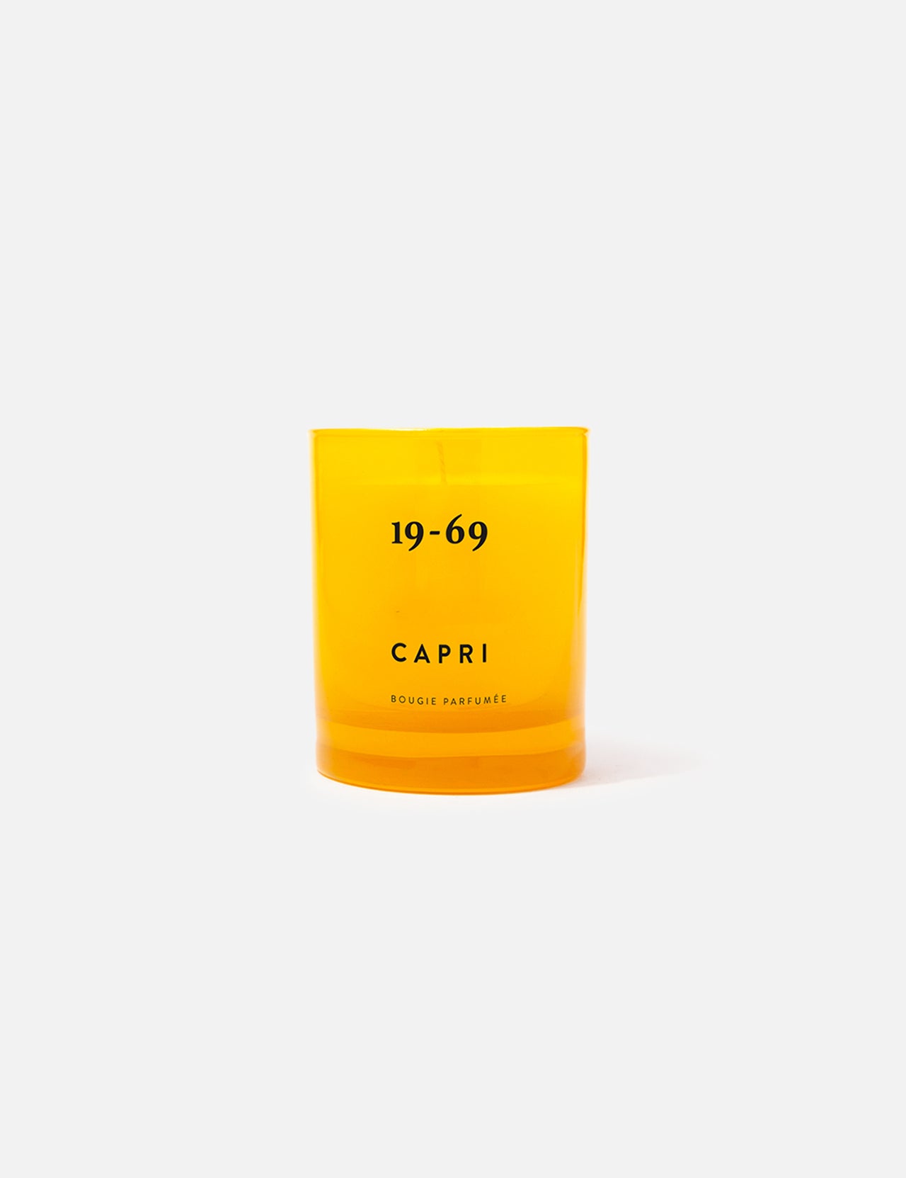 The 19-69 Capri Candle is a bright yellow fragrance candle in a glass holder with Capri branding, featuring an orange blossom scent and displayed on a plain light gray background.