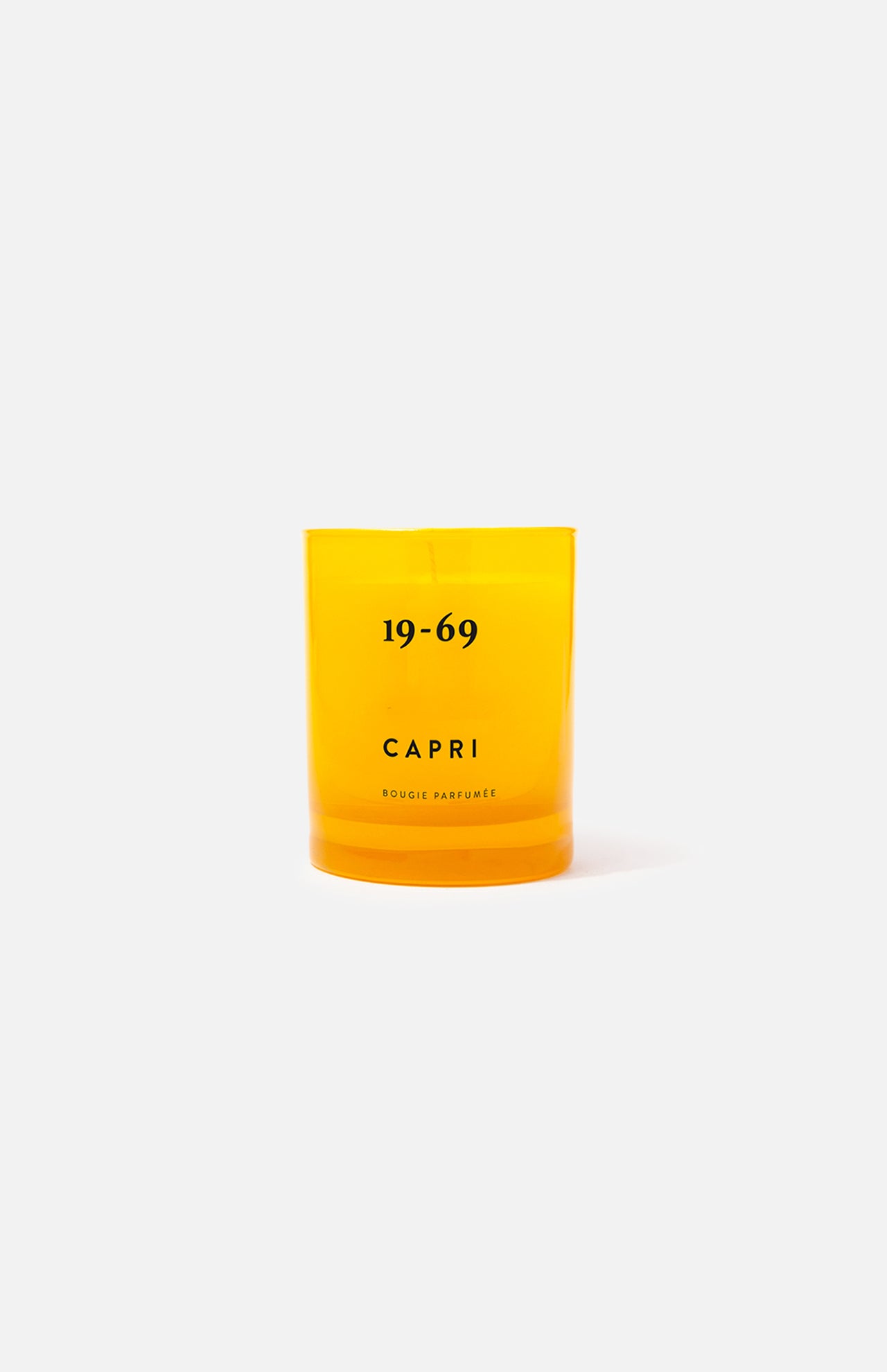 The 19-69 Capri Candle is a bright yellow fragrance candle in a glass holder with Capri branding, featuring an orange blossom scent and displayed on a plain light gray background.