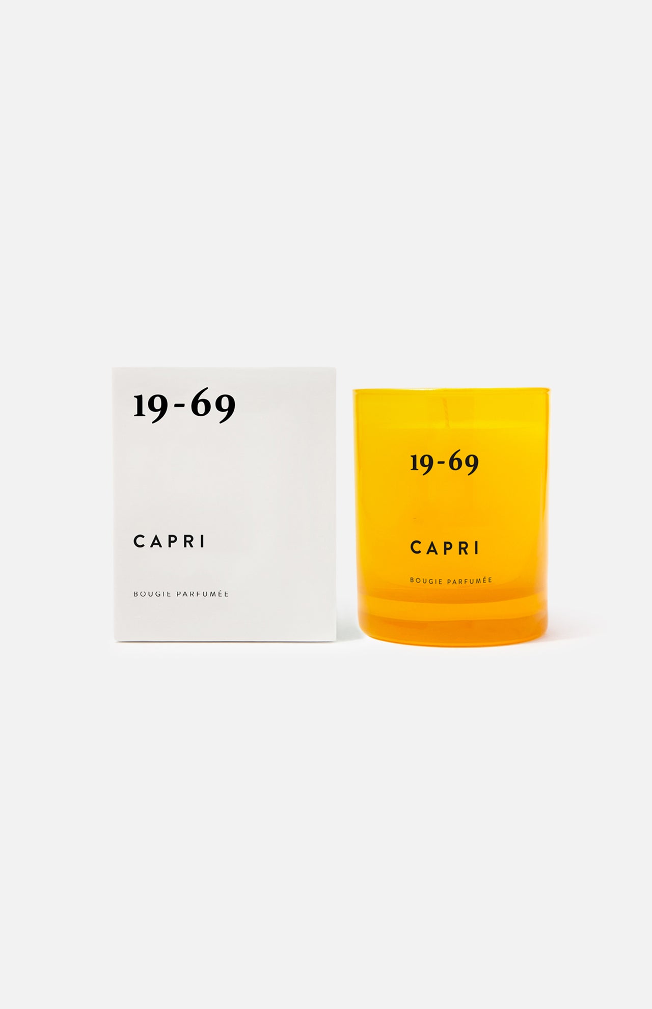 A white box and a yellow candle holder, both labeled 19-69 Capri Candle. The box is on the left, the holder on the right—set against a plain white background to evoke the fresh allure of Capri by 19-69.
