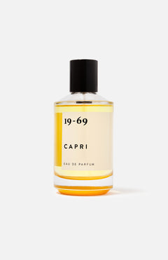 The 19-69 Capri EDP 100 ml Fragrance features a clear glass bottle with a black cap, filled with light yellow liquid. Displayed against a white background, this scent is inspired by Capri and highlighted by orange blossom notes.