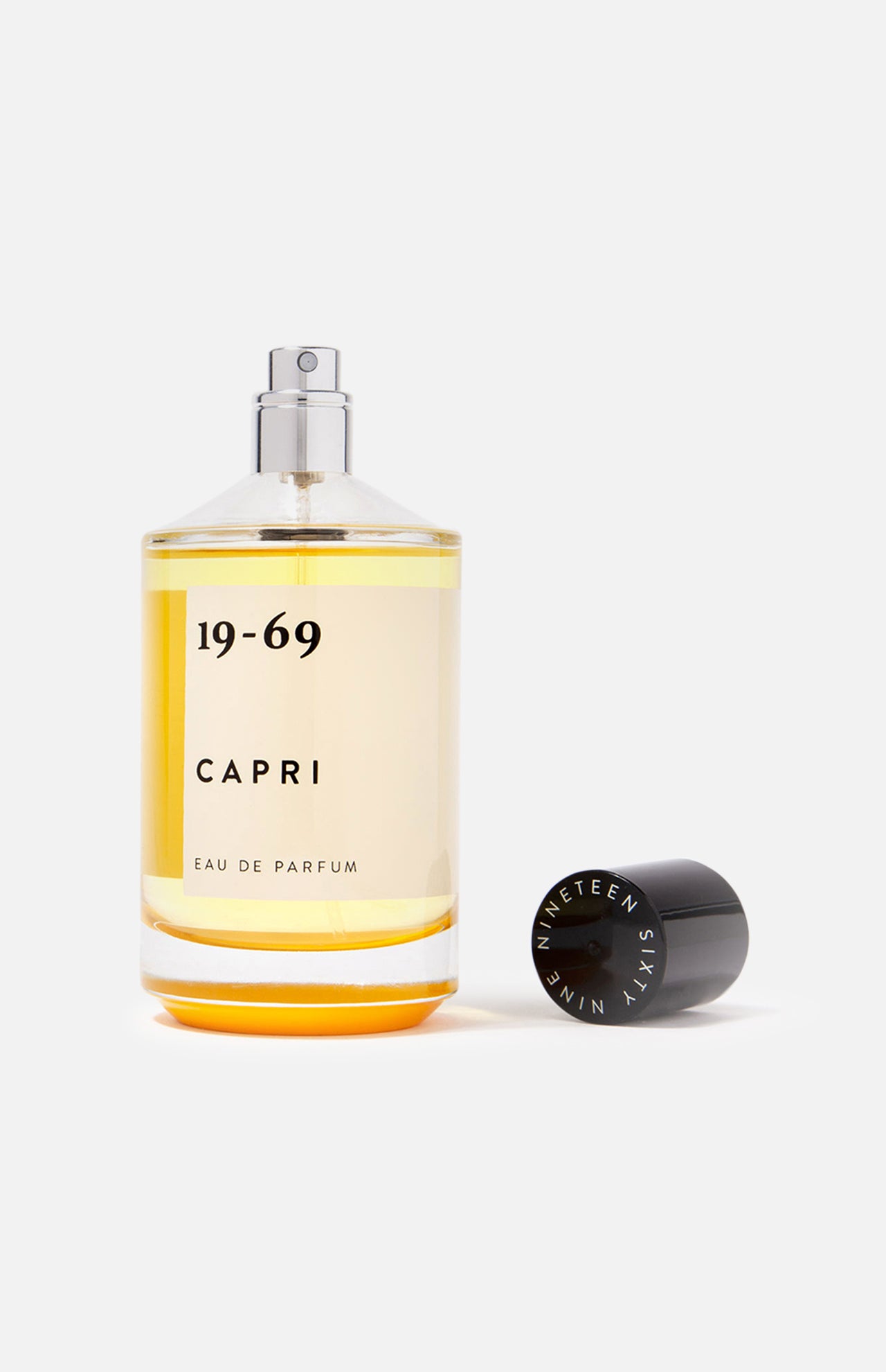 A clear 100 ml bottle of 19-69 Capri EDP Fragrance with golden liquid is shown on a white background, its black cap placed beside it and the spray nozzle exposed.