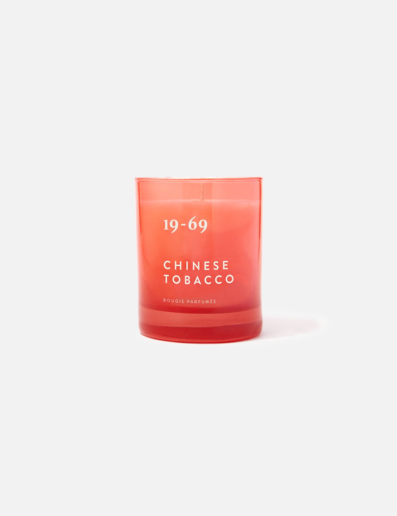 A red glass 19-69 Chinese Tobacco Candle sits upright on a plain white background, evoking a spicy woody scent inspired by Kuala Terengganu.