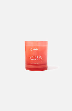 A red glass 19-69 Chinese Tobacco Candle sits upright on a plain white background, evoking a spicy woody scent inspired by Kuala Terengganu.