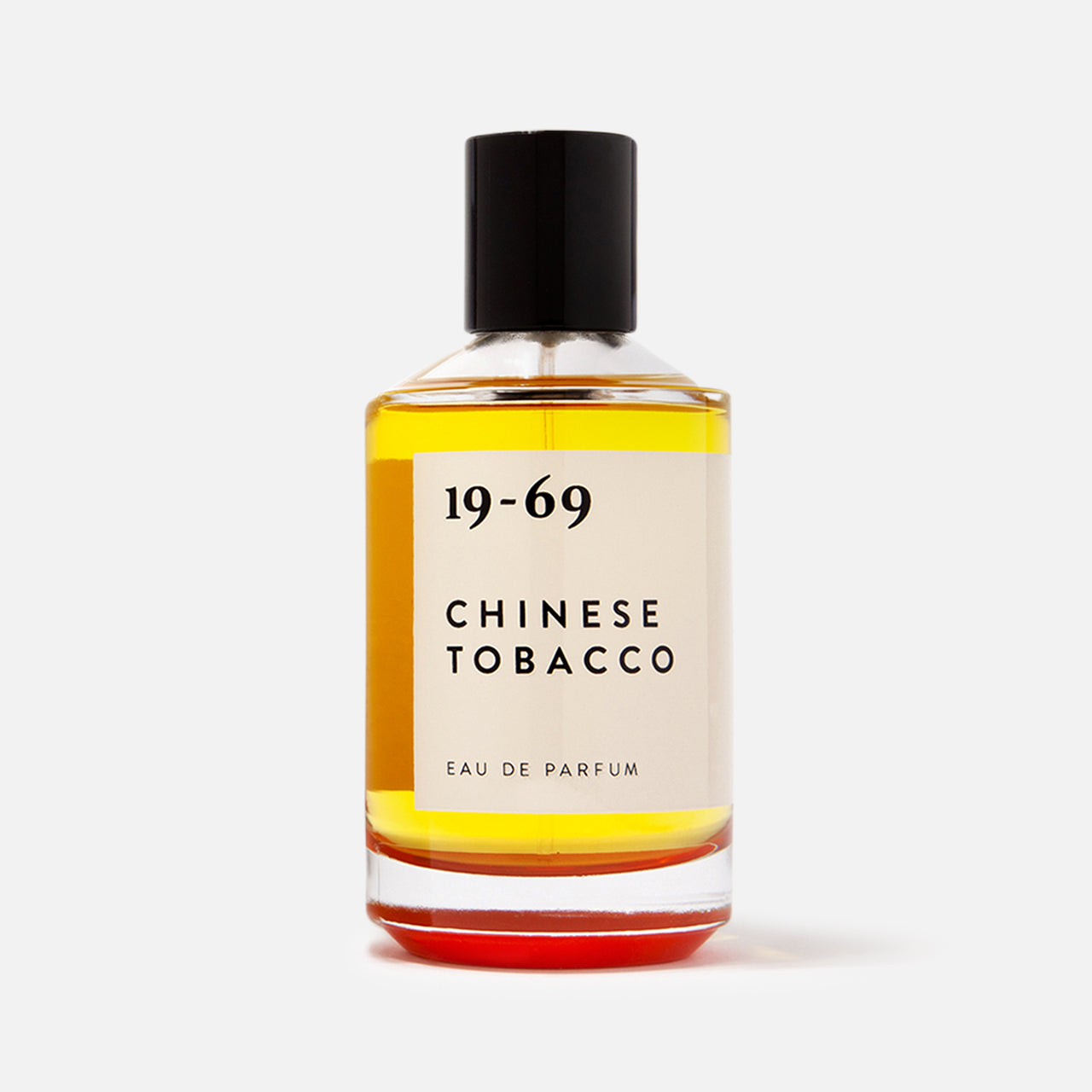 A clear 100ml glass bottle of 19-69 Chinese Tobacco EDP with a black cap, featuring amber liquid, sits against a white background. This unisex fragrance delivers a spicy woody scent that captivates the senses.