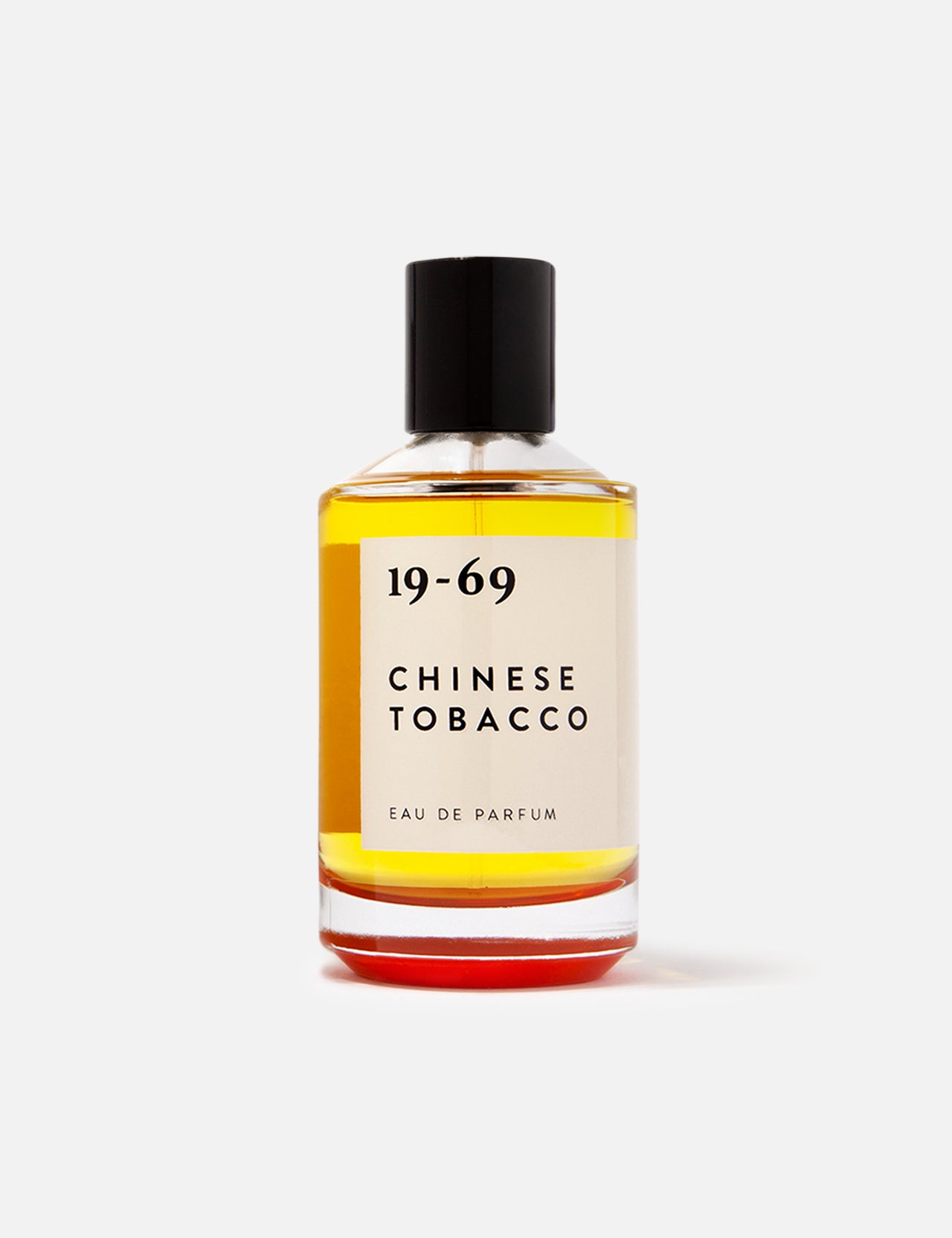 A clear 100ml glass bottle of 19-69 Chinese Tobacco EDP with a black cap, featuring amber liquid, sits against a white background. This unisex fragrance delivers a spicy woody scent that captivates the senses.