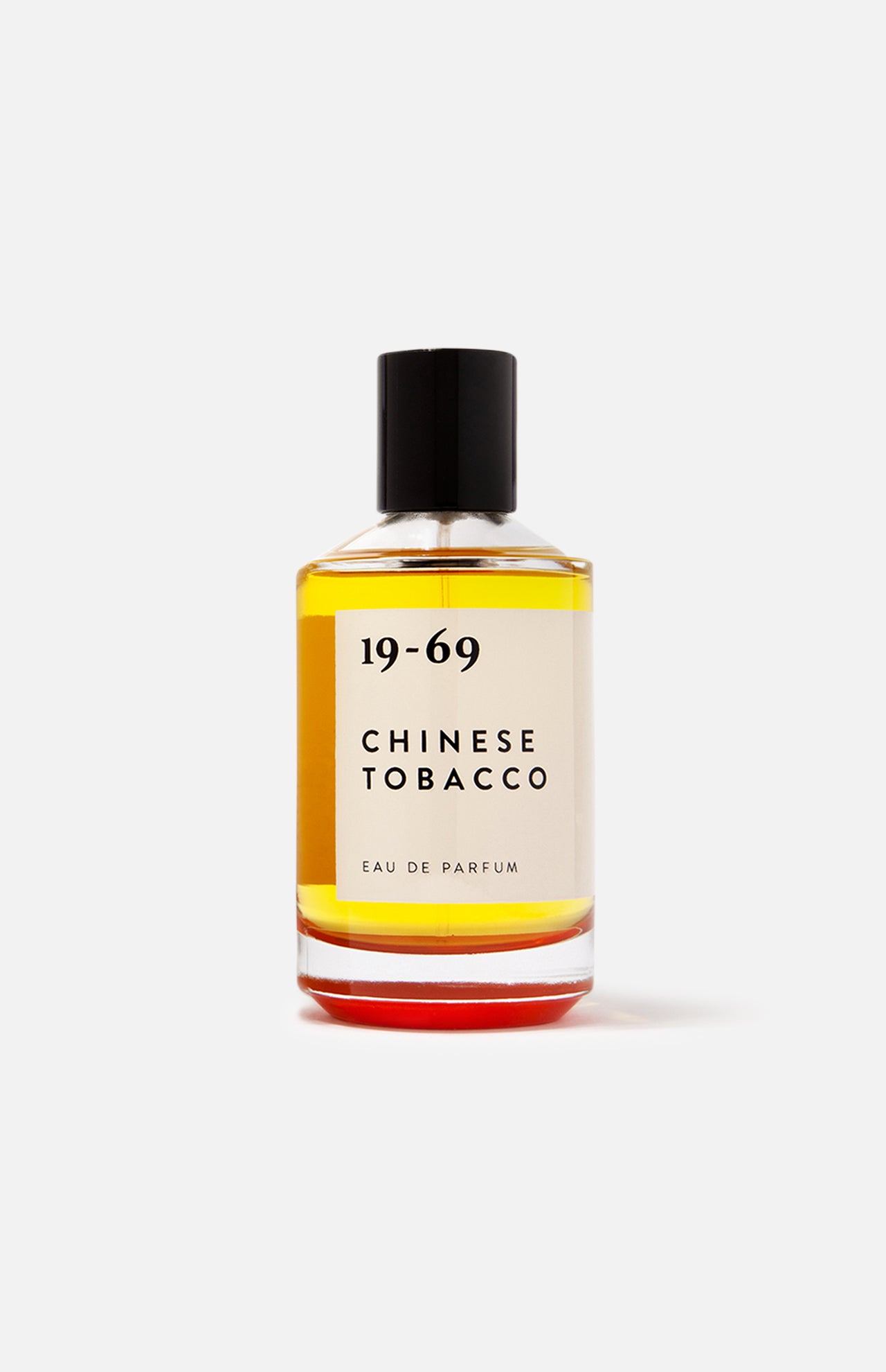 A clear 100ml glass bottle of 19-69 Chinese Tobacco EDP with a black cap, featuring amber liquid, sits against a white background. This unisex fragrance delivers a spicy woody scent that captivates the senses.