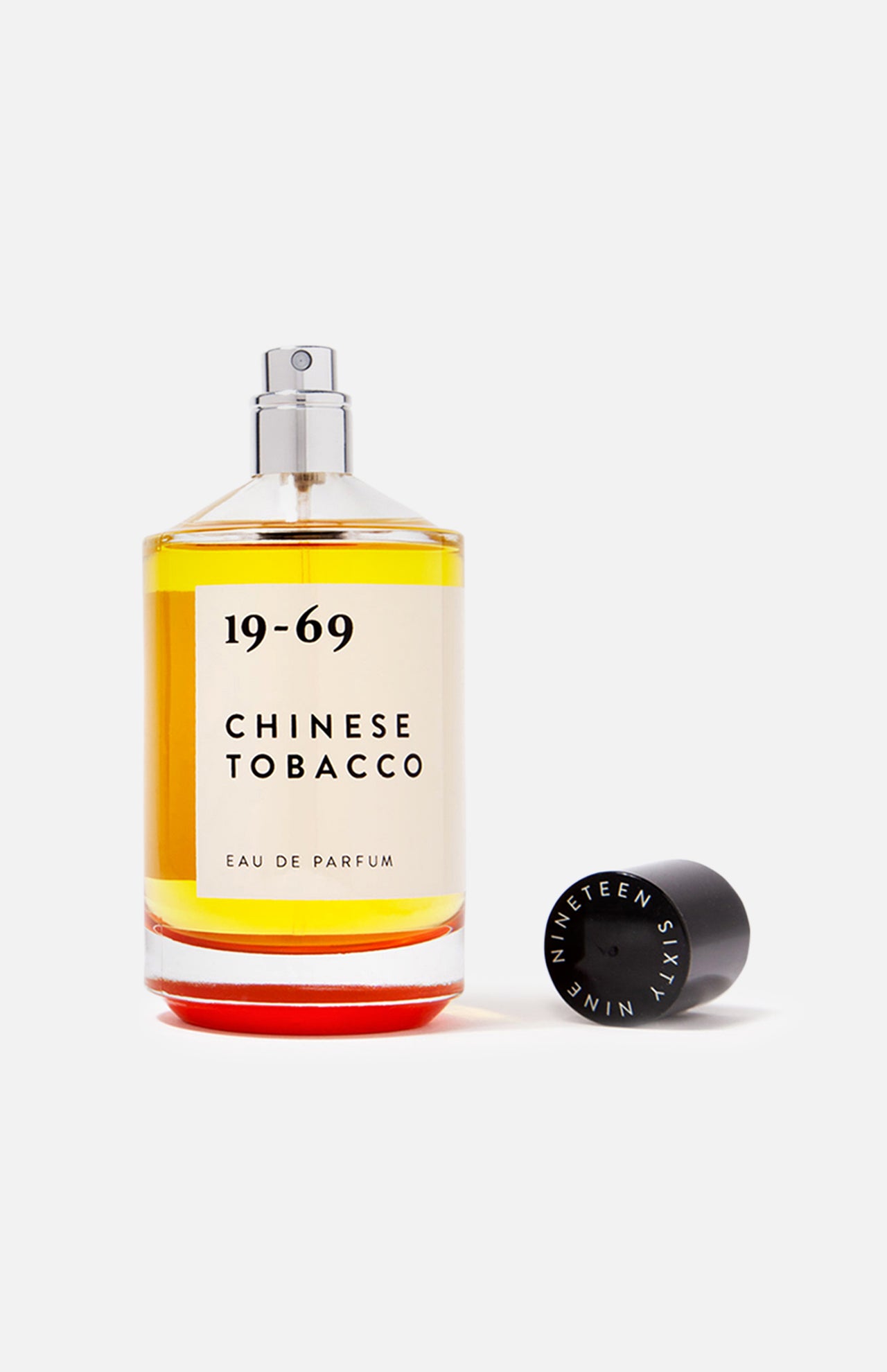 A clear glass bottle of 19-69 Chinese Tobacco EDP 100 ml Fragrance, featuring a Malaysia-inspired spicy woody scent with orange liquid, sits beside its black cap on a white background.