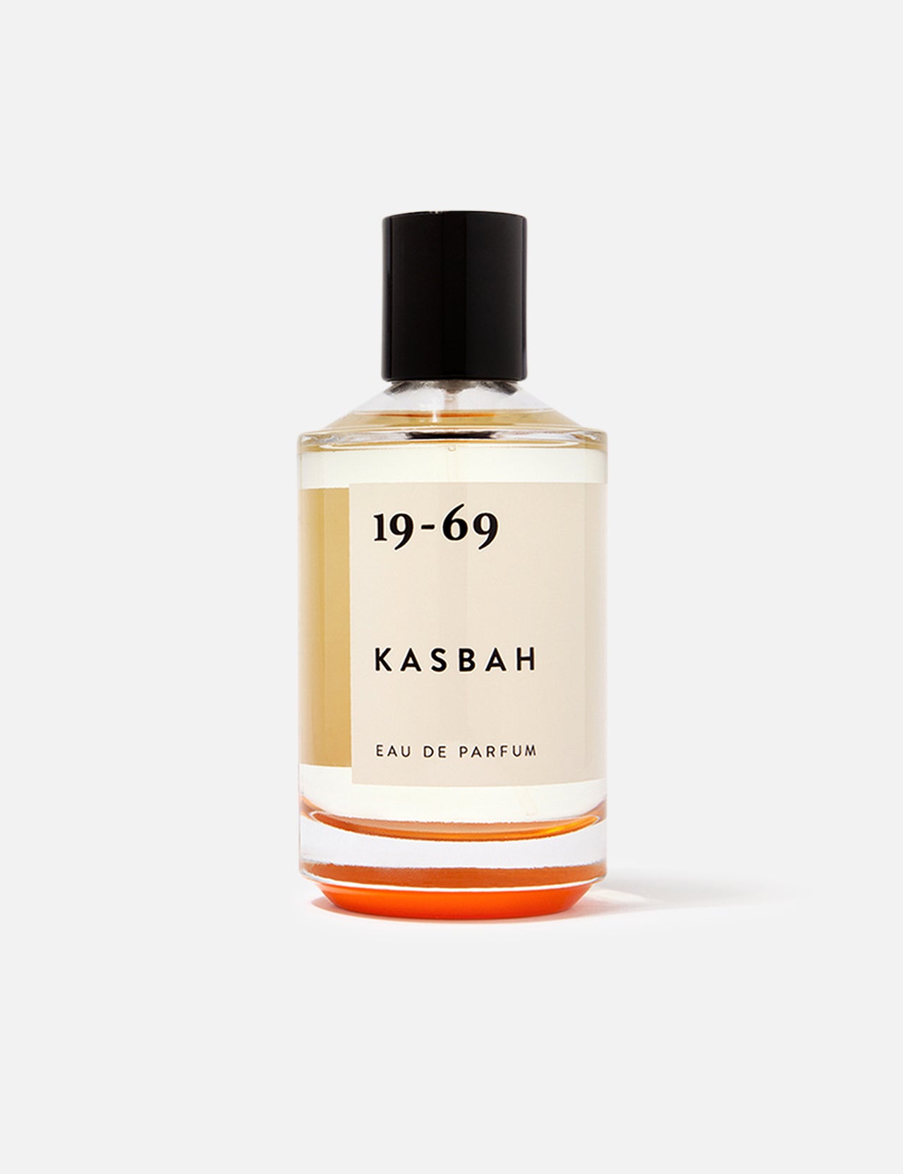 A clear glass bottle of 19-69 Kasbah EDP 100 ml Fragrance, a unisex scent with oriental spices and sandalwood, features light amber liquid, a black cap, and minimalist black text on a cream label against a plain white background.