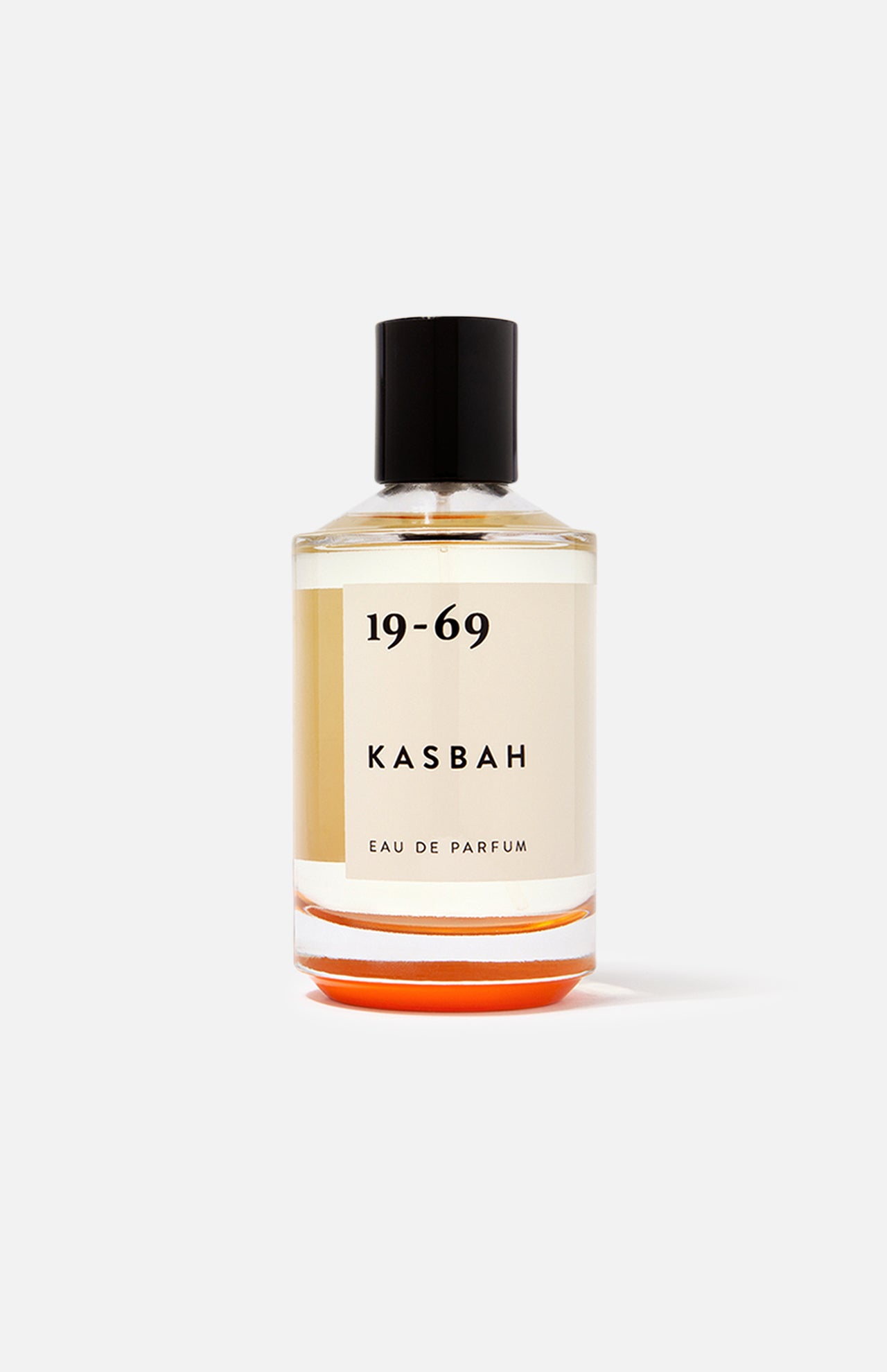 A clear glass bottle of 19-69 Kasbah EDP 100 ml Fragrance, a unisex scent with oriental spices and sandalwood, features light amber liquid, a black cap, and minimalist black text on a cream label against a plain white background.