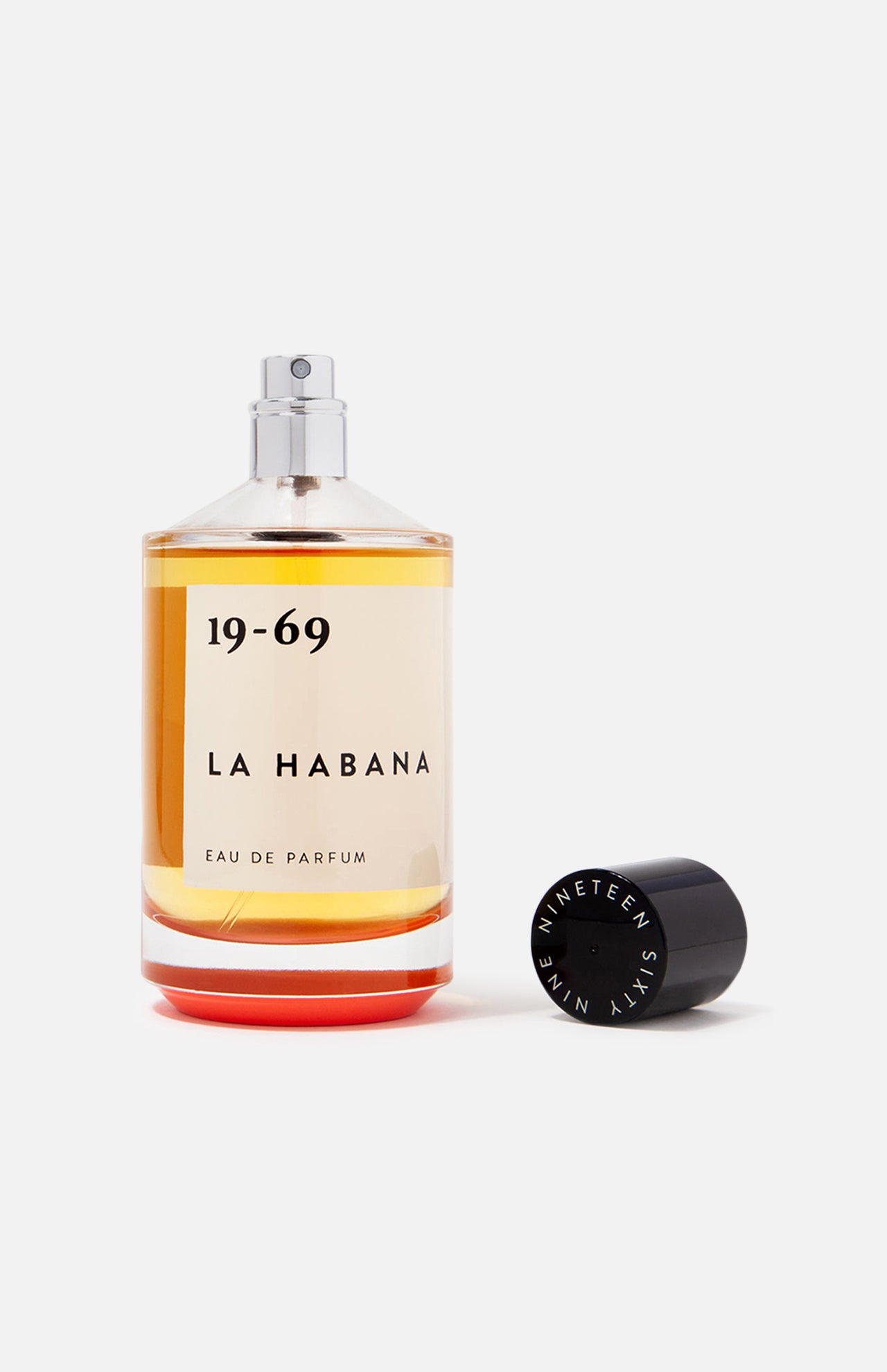 A clear glass bottle of 19-69 La Habana EDP 100 ml Fragrance shows amber liquid inside. The unisex scent evokes Havana, and the black cap marked NINETEEN SIXTY NINE sits beside the bottle on a white background.