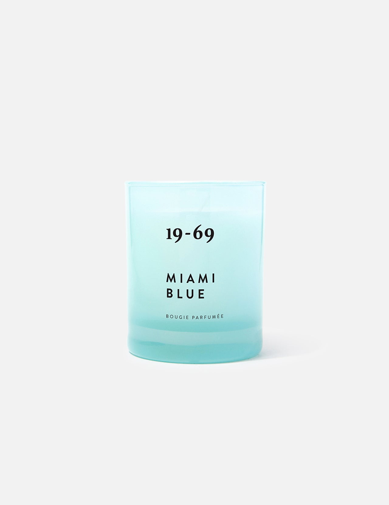 A turquoise blue 19-69 Miami Blue Candle sits on a plain light gray background, evoking a fresh aquatic scent inspired by Miami.