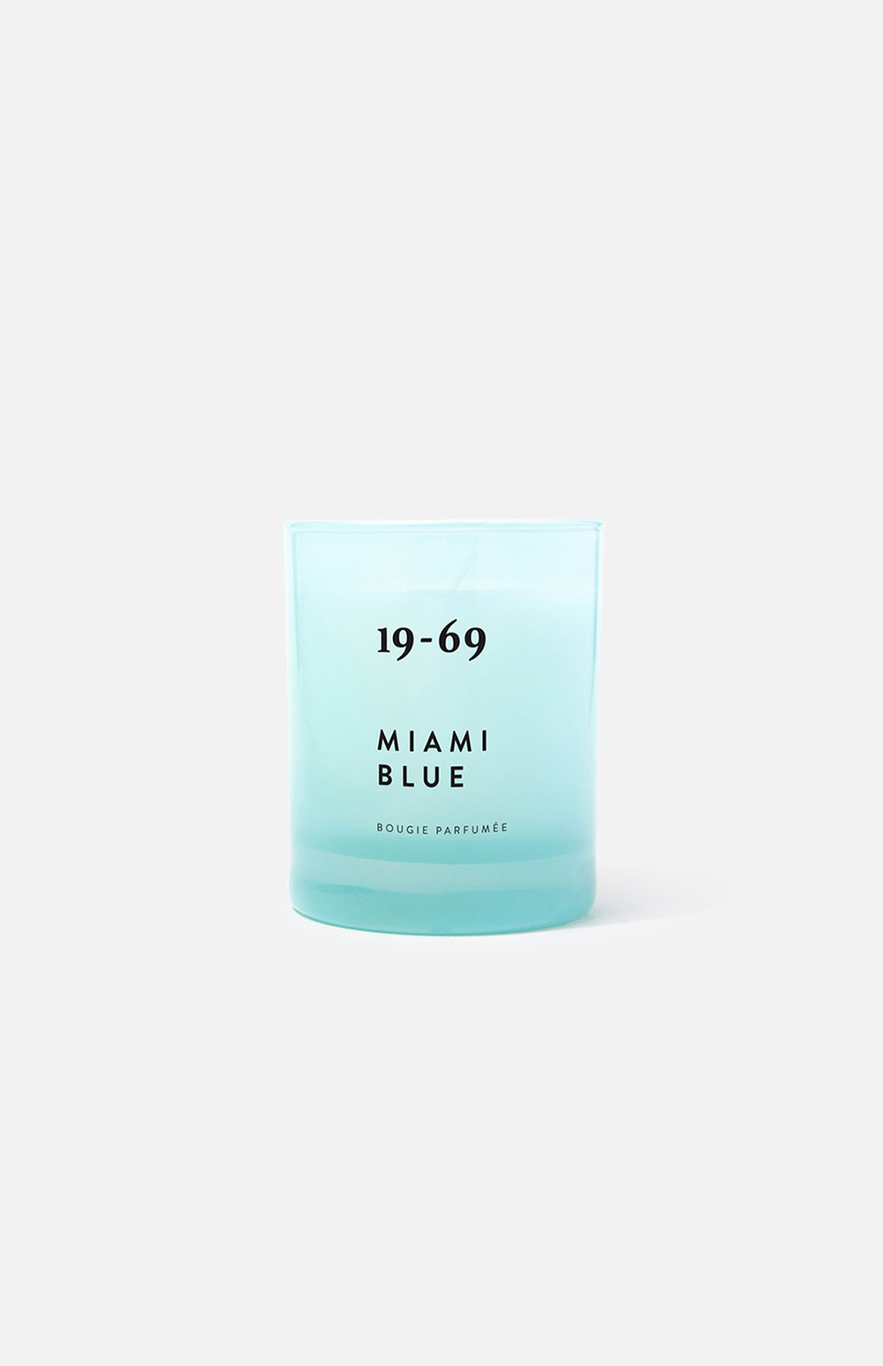 A turquoise blue 19-69 Miami Blue Candle sits on a plain light gray background, evoking a fresh aquatic scent inspired by Miami.