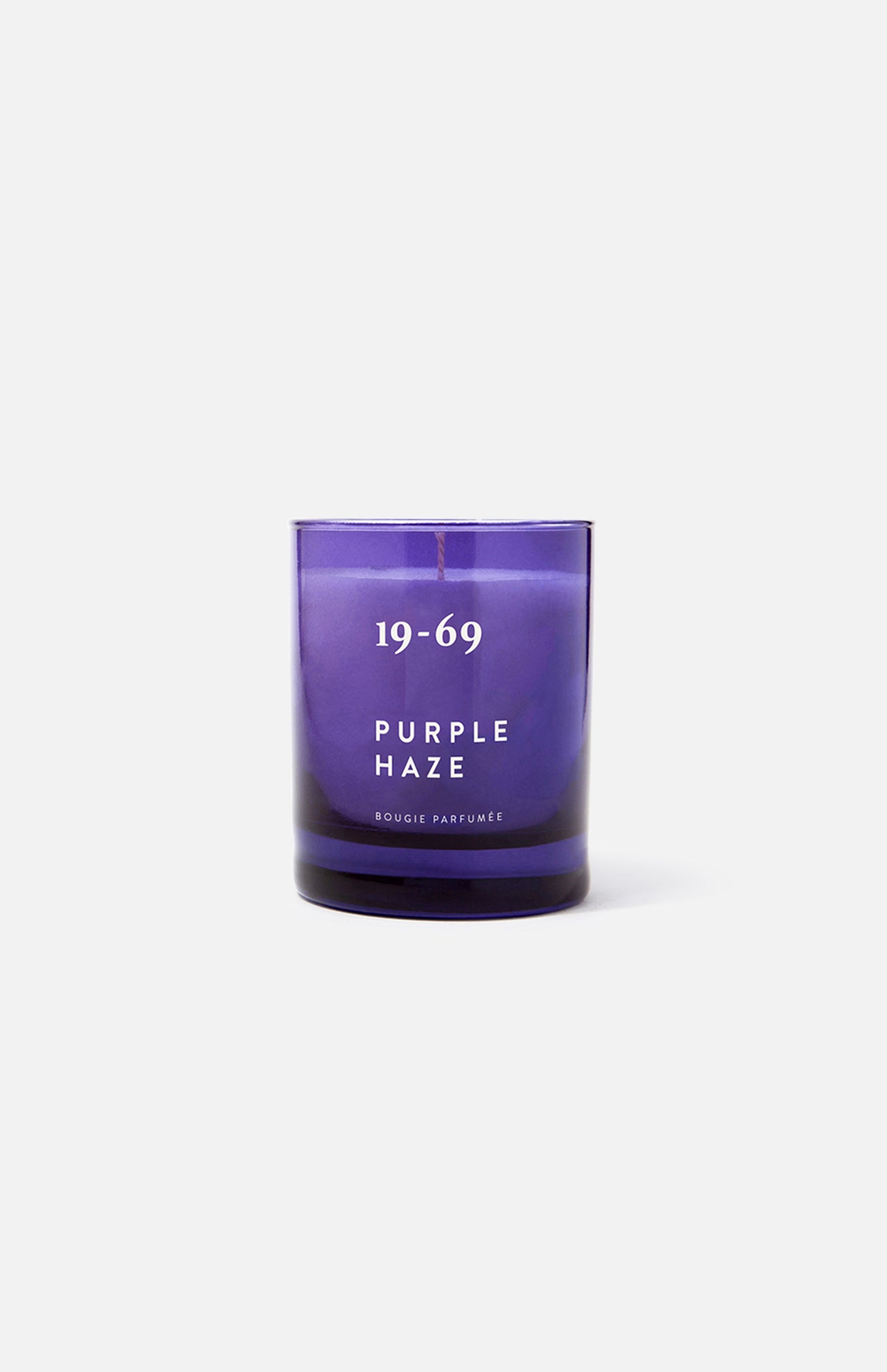 The 19-69 Purple Haze Candle, inspired by Woodstock and featuring Italian bergamot notes, is shown in a purple glass vessel against a plain white background.