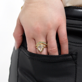 A hand with a LOGAN HOLLOWELL Enigma Channel Band Ring in yellow gold rests on the back pocket of black pants, paired with a cream-colored top—showcasing refined designer jewelry style.