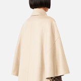 Back view of a person wearing a beige MAX MARA Cashmere Button Sleeve Cape Jacket with a double-breasted silhouette and button detailing on the sleeves over a dark brown long-sleeve top and blue jeans.