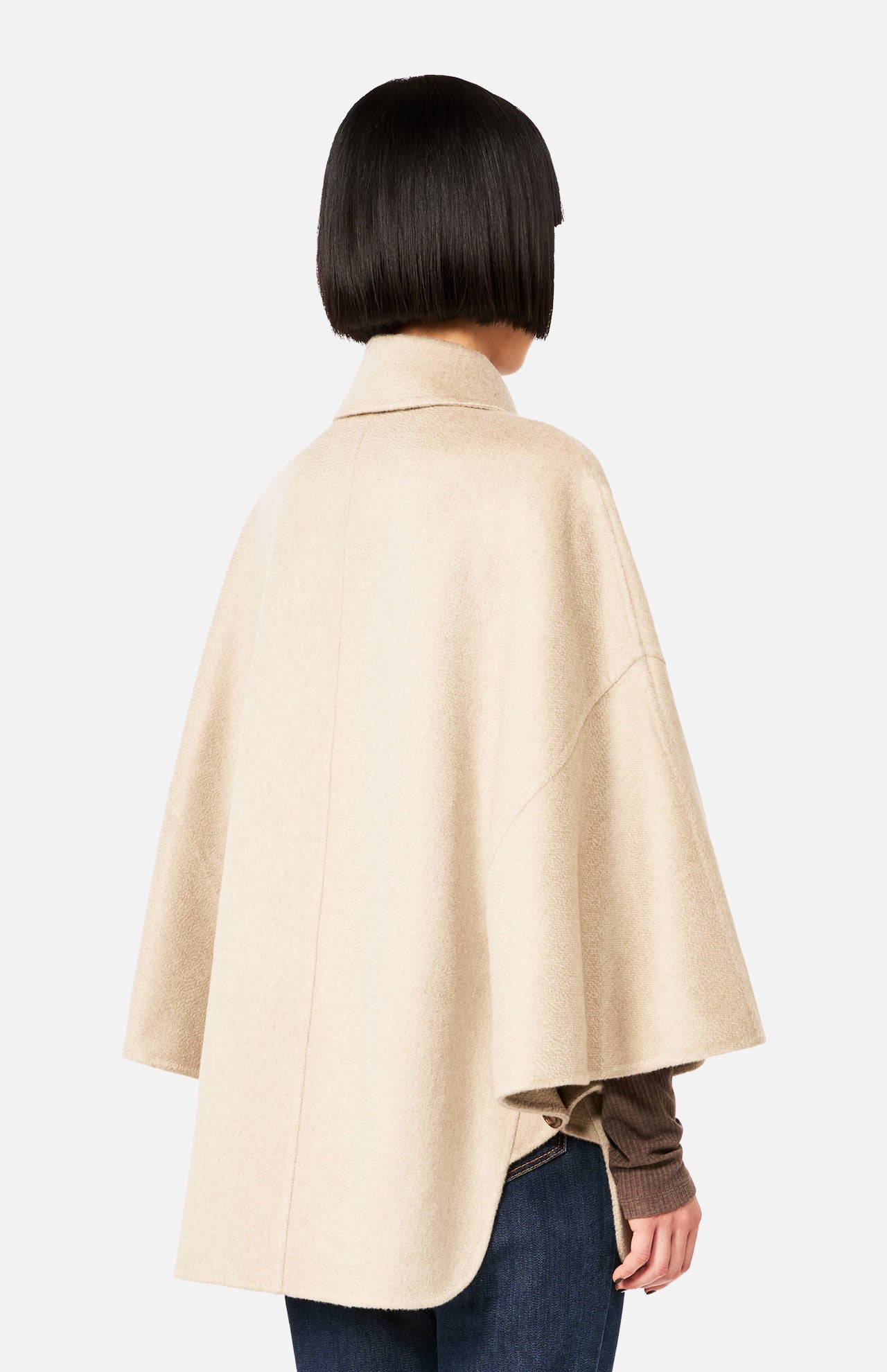 Back view of a person wearing a beige MAX MARA Cashmere Button Sleeve Cape Jacket with a double-breasted silhouette and button detailing on the sleeves over a dark brown long-sleeve top and blue jeans.