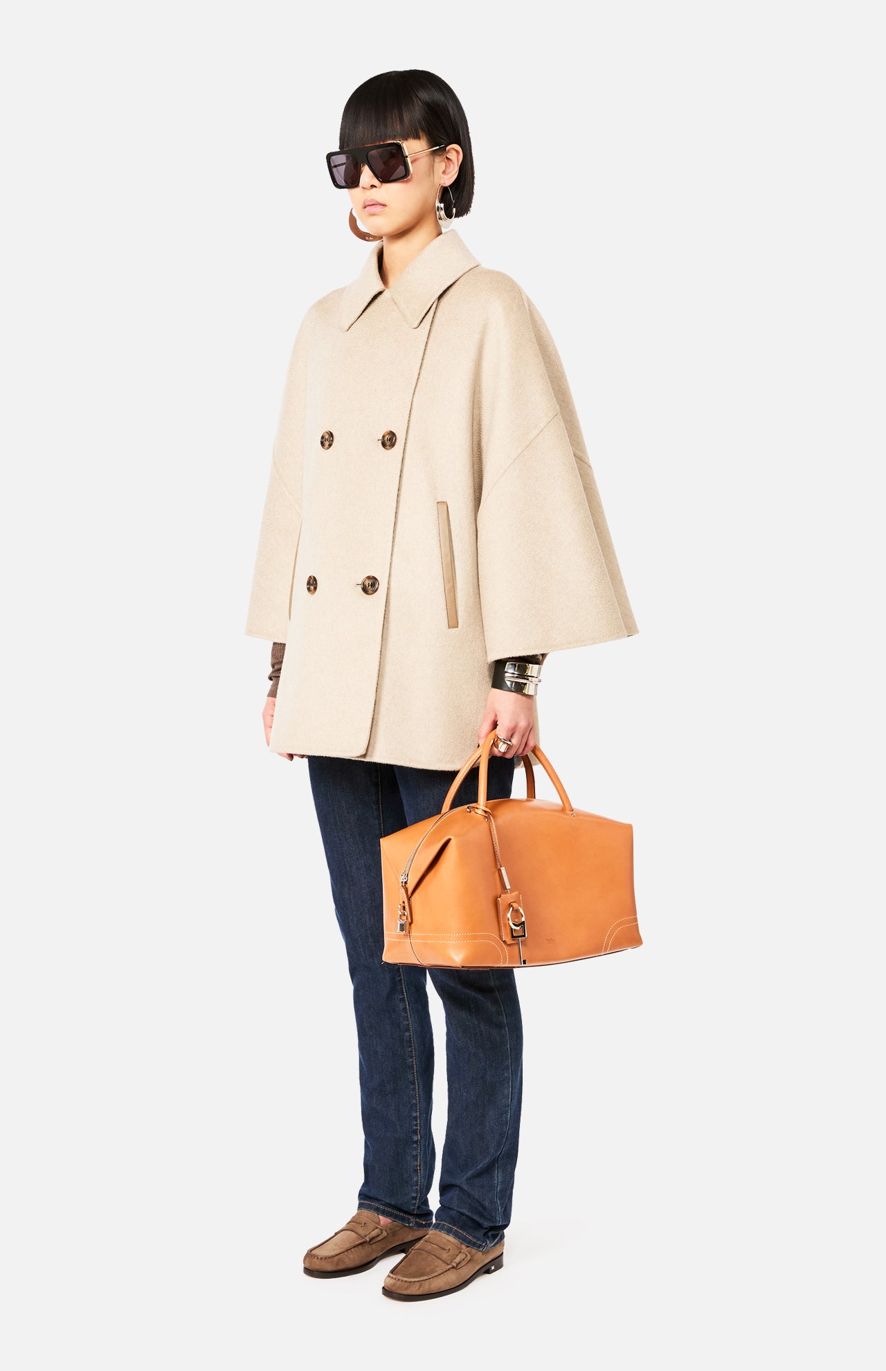 A person wearing a beige Max Mara Cashmere Button Sleeve Cape Jacket, dark jeans, and brown loafers, carrying a tan leather handbag.