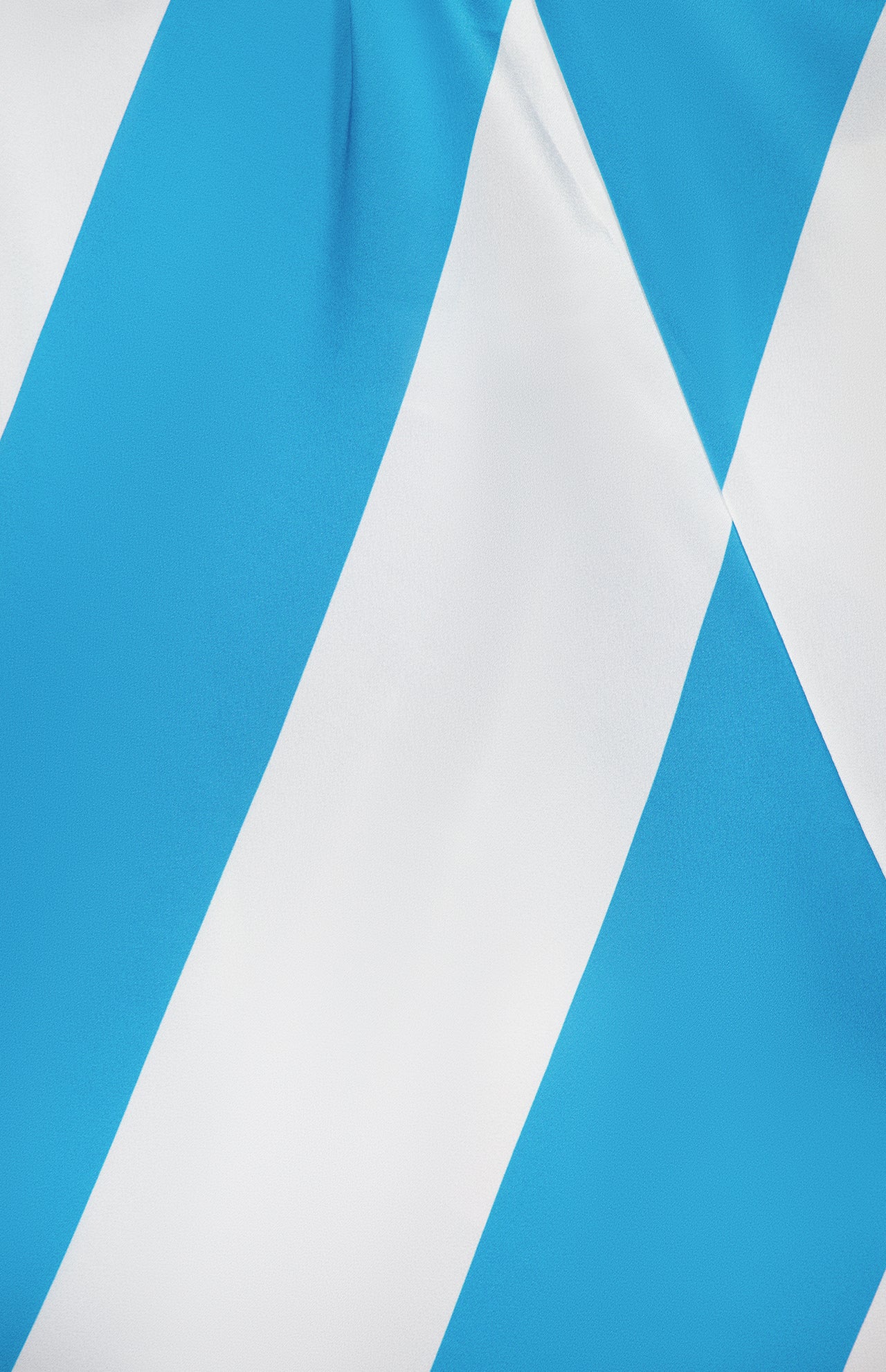 A close-up of the Chantell Striped Satin Maxi Dress by RONNY KOBO shows its blue and white diagonal stripes, reminiscent of the Bavarian flag, with a slightly wrinkled texture adding depth to this stylish piece.
