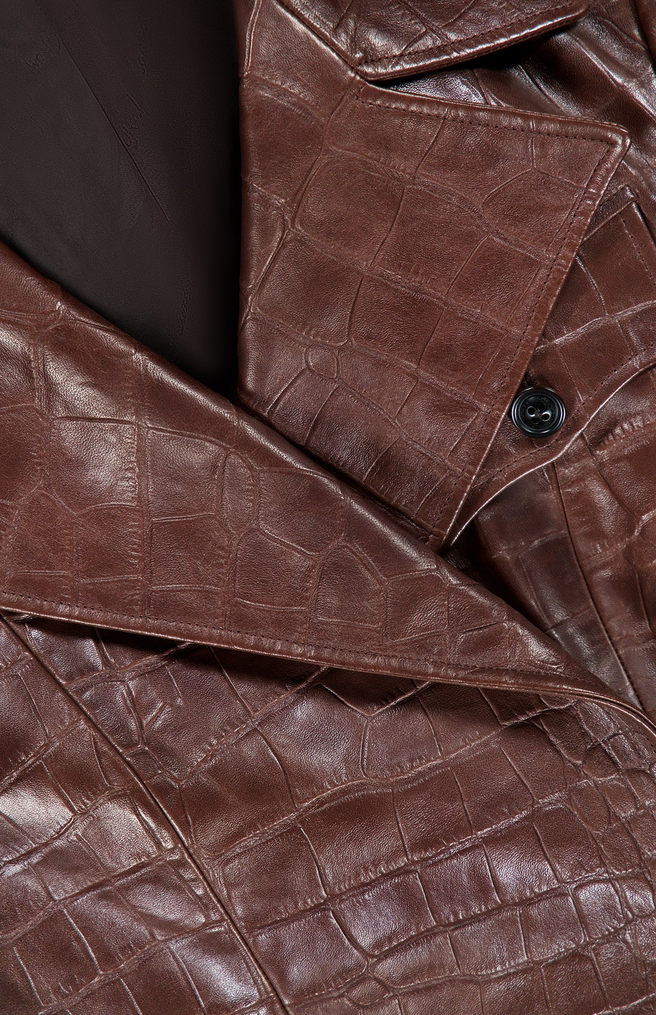 Close-up of the Jaxson Leather Moto Jacket from RALPH LAUREN COLLECTION, made of brown crocodile-patterned lambskin leather, highlighting its visible collar, lapel, and signature black button—an ode to the refined craftsmanship synonymous with Ralph Lauren.