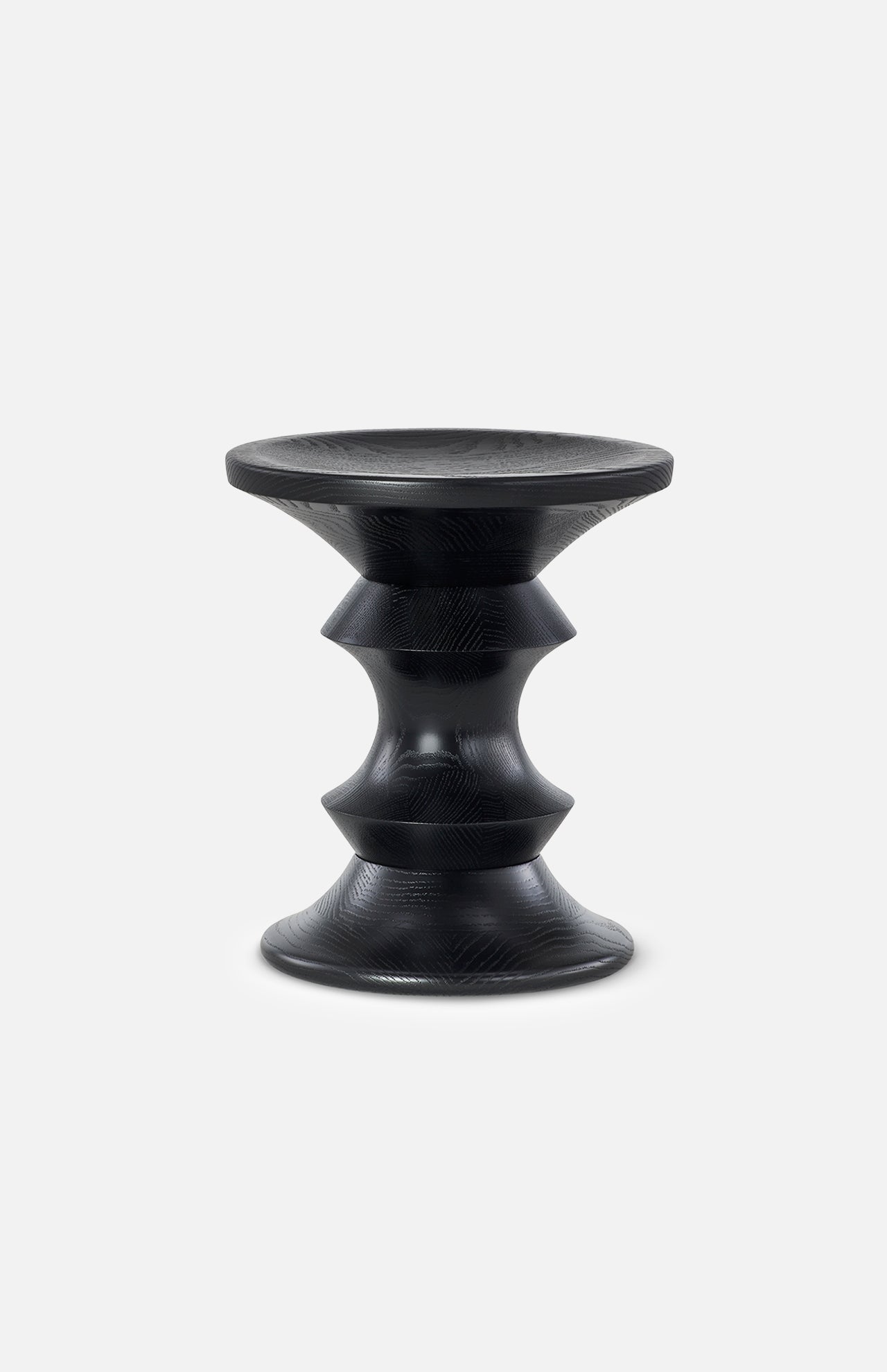 The Eames Turned Stool, Shape A by HERMAN MILLER is a small black hourglass-shaped stool with smooth sculptural lines and subtle textured patterns, inspired by the classic Eames walnut stool, shown on a plain light gray background.