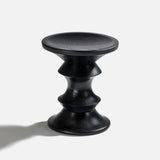 The HERMAN MILLER Eames Turned Stool, Shape A, features a black finish with a round top and base, three wavy concave midsections in solid walnut style, and casts a leftward shadow on a plain light background.
