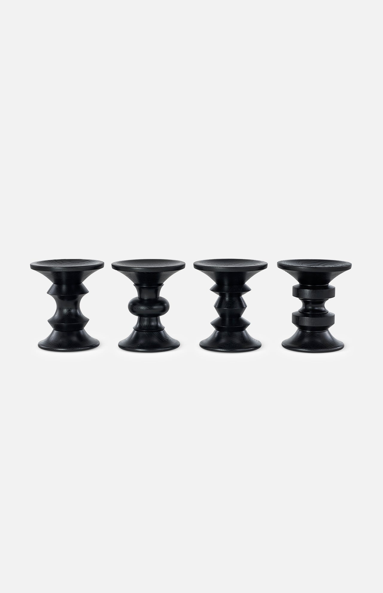 Four HERMAN MILLER Eames Turned Stools, Shape A—black, uniquely contoured cylinders inspired by the iconic Eames walnut stool—are evenly spaced in a row against a plain white background.